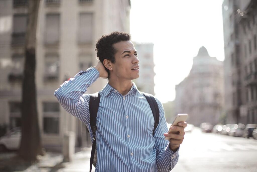 Traveller holding phone while looking around the city. Find the best phone plans for travelling.